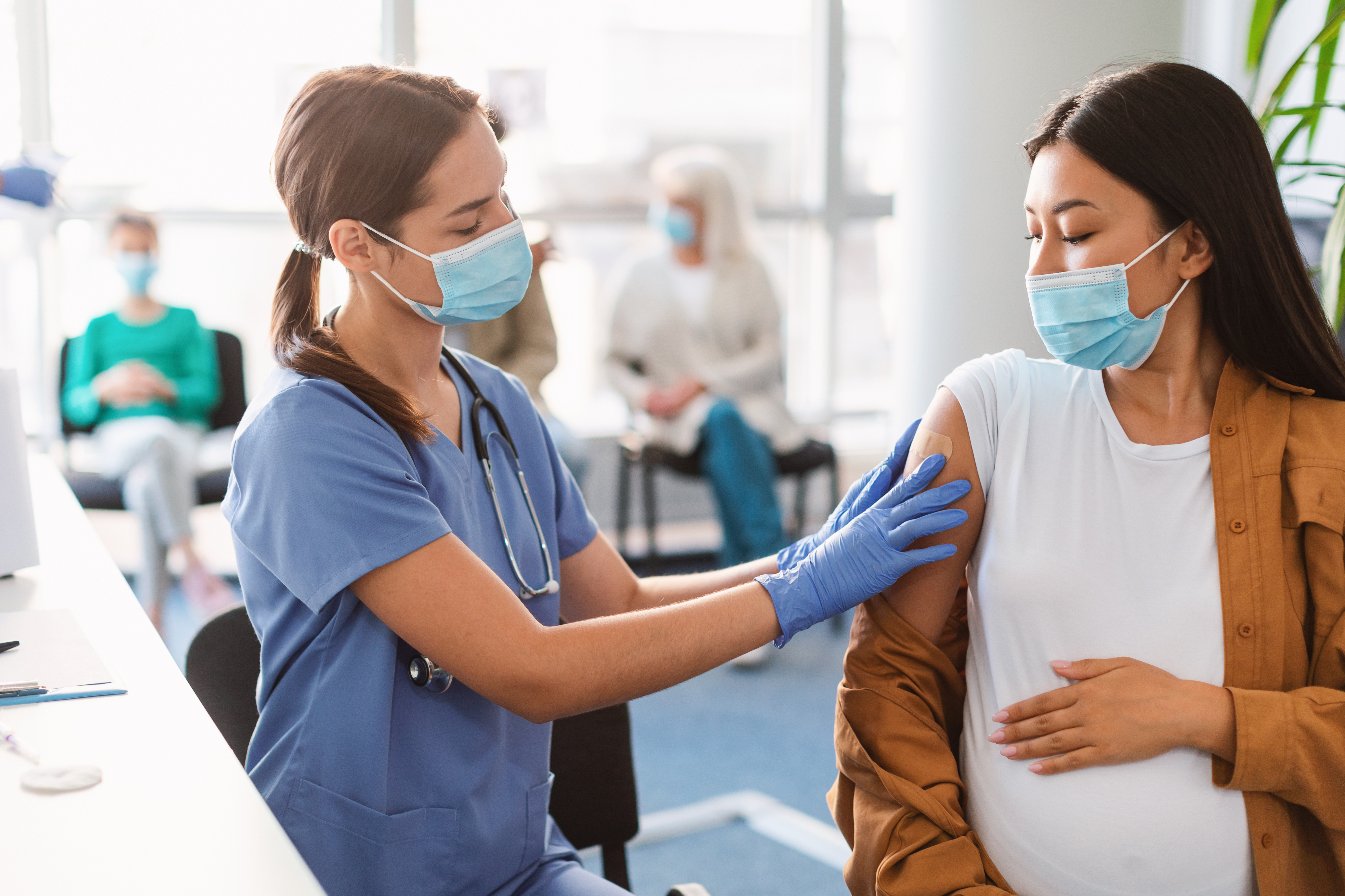 Zorgmedewerker vaccineert zwangere vrouw met mondkapje